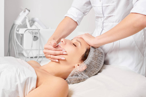 Kosmetolog wcierający krem nawilżający w skórę twarzy kobiety w celu odmłodzenia, zabieg przeciwzmarszczkowy w salonie spa. kosmetyczka ręce stosując krem do twarzy dla kobiet pielęgnacji skóry - Zdjęcie, obraz