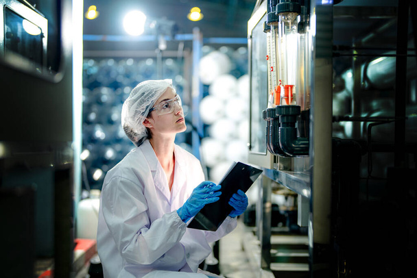 tudós munkás ellenőrzi a fordított ozmózis gép rendszer minőségét az ipari gyárban. A női munkavállaló adatai a vezérlőpultnál, a hordozható üzem újrahasznosítására nehezedő nyomás mérésével. - Fotó, kép