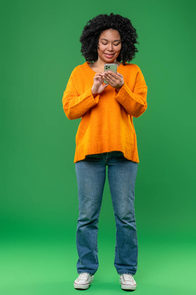 Communication. Curly-haired young woman in orange with a smartphone in hands - Fotografie, Obrázek