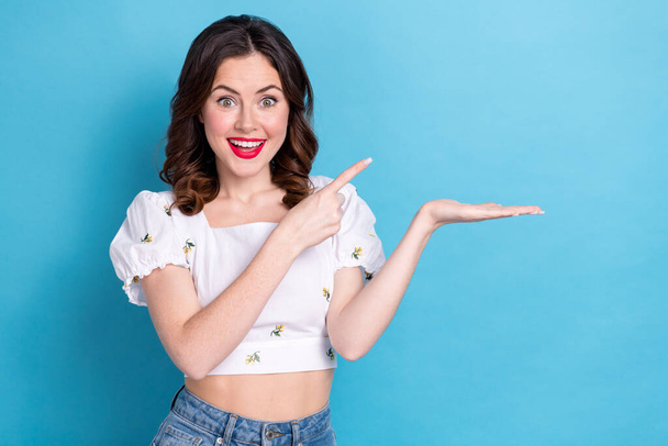 Photo of pretty excited lady wear white blouse showing finger holding arm empty space isolated blue color background. - Zdjęcie, obraz