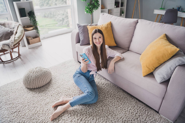 Foto de linda adorable chica joven usar camisa a rayas sofá sentado charlando gadget moderno en el interior de la habitación del apartamento. - Foto, imagen