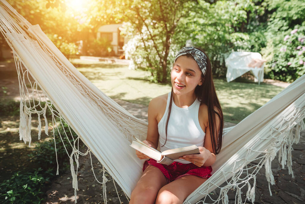 Счастливая девушка-хиппи читает книгу в гамаке, весело играя в трейлере кемпера. Отдых, отпуск, поездка. - Фото, изображение