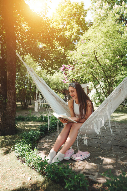 Onnellinen hippi tyttö lukee kirjaa riippumatossa, jolla on hauskaa leikkiessään asuntovaunussa. Loma, loma, matka käsite. Laadukas valokuva - Valokuva, kuva