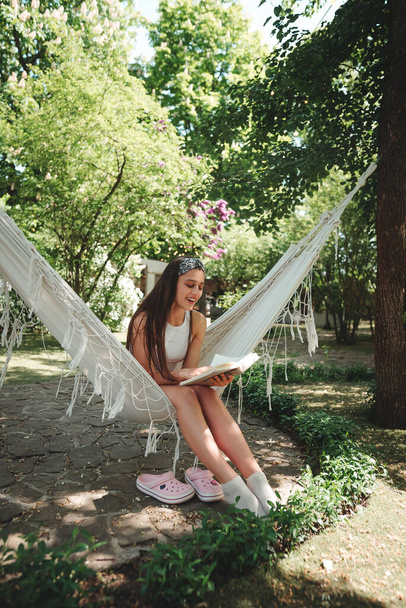 Happy hippie girl is reading a book in hammock having a good time with playing in camper trailer. Holiday, vacation, trip concept.High quality photo - Photo, Image