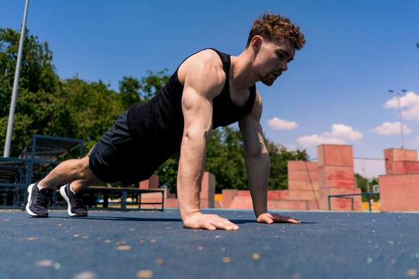 young pumped-up athlete doing push-ups from the ground during street training endurance exercise swings arms shoulders - Foto, imagen