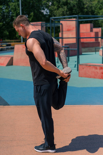 portrait of a young sportsman with tattoos doing warm-up exercises outdoors street training on sports ground motivation - Fotoğraf, Görsel