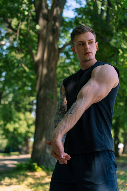 portré egy fiatal sportolóról tetoválásokkal, aki bemelegítő gyakorlatokat végez a szabadban utcai edzés a park motivációjában - Fotó, kép