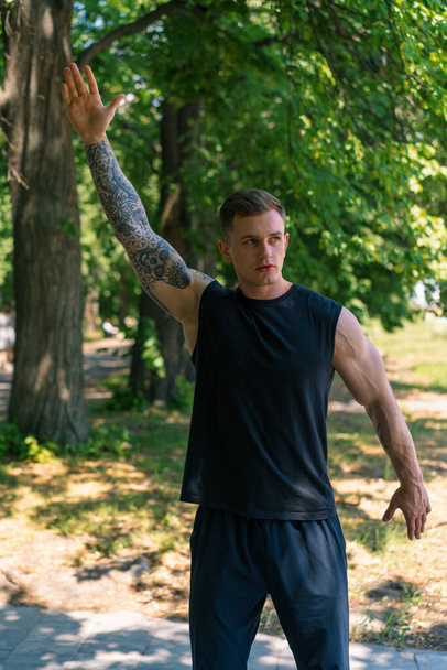 портрет молодого спортсмена с татуировками, занимающегося разминкой на улице, тренирующегося в парковой мотивации - Фото, изображение