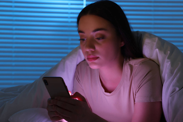 Молода жінка використовує сучасний смартфон у ліжку вночі. Інтернет залежність
 - Фото, зображення