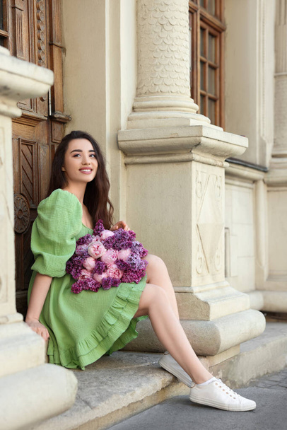Beautiful woman with bouquet of spring flowers near building outdoors, space for text - Φωτογραφία, εικόνα