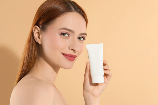 Beautiful young woman holding sun protection cream on beige background, space for text - Fotó, kép