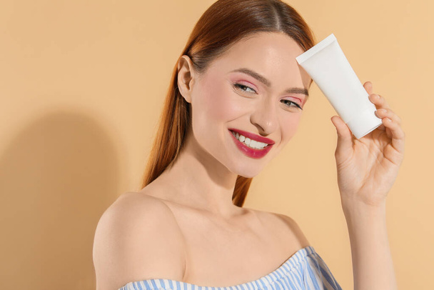 Beautiful young woman holding sun protection cream on beige background - 写真・画像