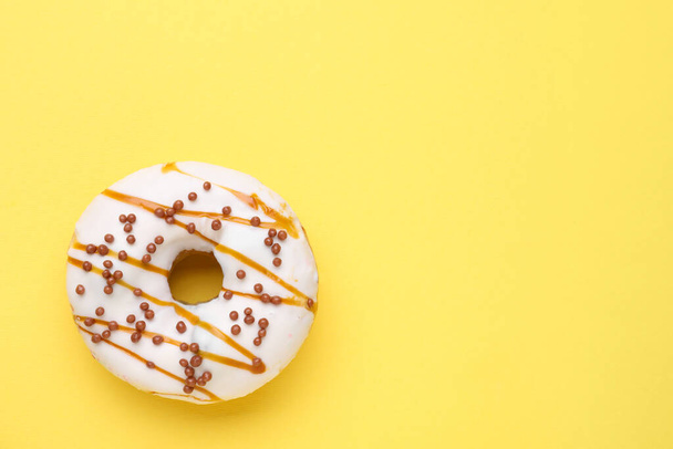 Tasty glazed donut decorated with sprinkles and caramel on yellow background, top view. Space for text - Φωτογραφία, εικόνα