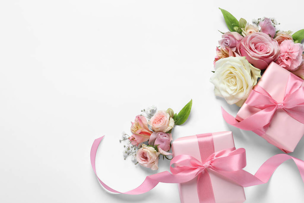 Gift boxes and beautiful flowers on white background, flat lay. Space for text - 写真・画像
