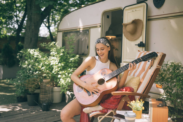 Gelukkig hippie meisje hebben een goede tijd met het spelen op gitaar in camper trailer. Vakantie, vakantie, reis concept.Hoge kwaliteit foto - Foto, afbeelding