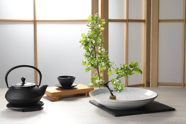Stylish ikebana as house decor. Beautiful fresh branch and tea set on wooden table - Foto, afbeelding