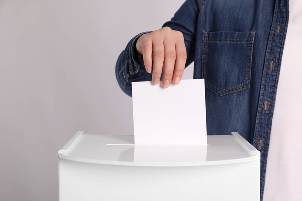 Woman putting her vote into ballot box on light grey background, closeup - Foto, Imagen
