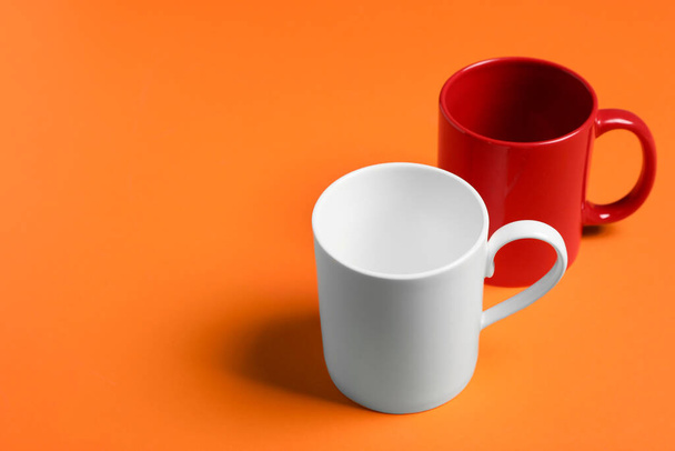 Red and white ceramic mugs on orange background, space for text - 写真・画像