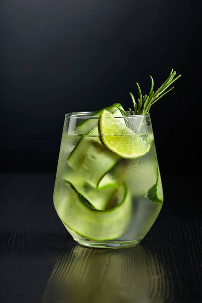 Gin tonic with ice, rosemary, lime, and cucumber in frosted glass. Glass with a cocktail on a black background. Copy space. - Foto, afbeelding