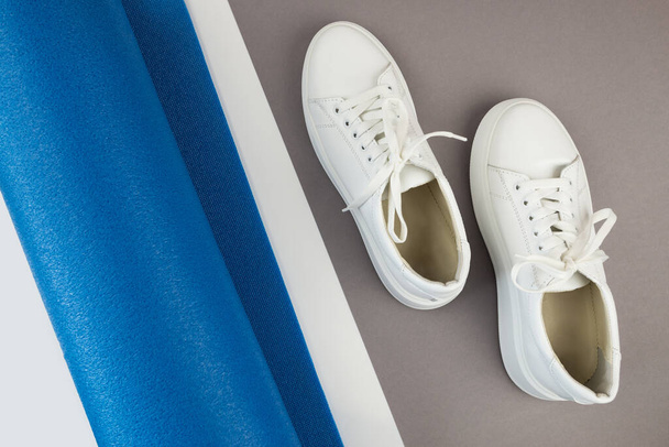 Top view photo of white sneakers and fitness mat. The concept of sport, yoga, fitness. - Photo, Image