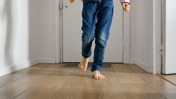 Πόδια μικρού αγοριού καθώς τρέχει κάτω από το μακρύ ξύλινο διάδρομο του σπιτιού του. Ευτυχισμένη παιδική ηλικία, εσωτερική παιχνίδι, και την ανάπτυξη των αναπτυξιακών δεξιοτήτων ενός παιδιού - Φωτογραφία, εικόνα