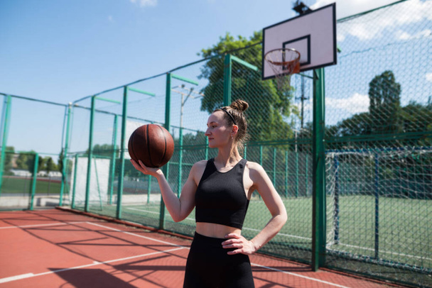 Young sports girl with a basketball on the basketball court outdoors, active weekend. - Foto, Imagem