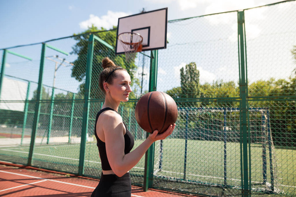 Jong sportmeisje met een basketbal op het basketbalveld buiten, actief weekend. - Foto, afbeelding