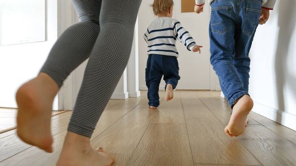 Großaufnahme von Mutter und zwei Jungen, die zu Hause auf dem Holzboden laufen. Konzept von Familienliebe, Freude und Spaß im Haushalt. - Foto, Bild