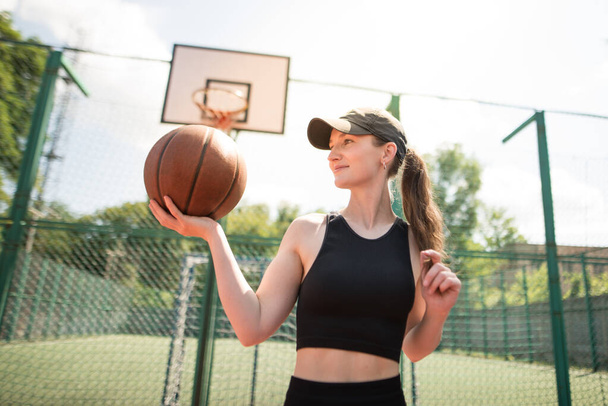 Młoda sportowa dziewczyna z koszykówką na boisku do koszykówki na świeżym powietrzu, aktywny weekend. - Zdjęcie, obraz