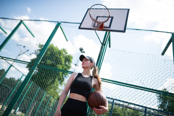 Joven chica deportiva con una pelota de baloncesto en la cancha de baloncesto al aire libre, fin de semana activo. - Foto, imagen