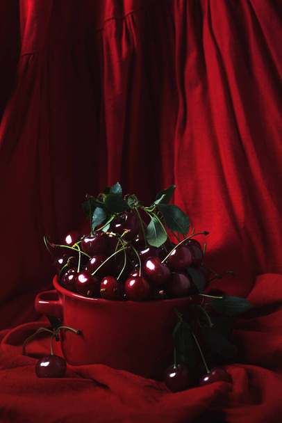 Ripe cherries in a red bowl on a red background. Photo in low key - Zdjęcie, obraz