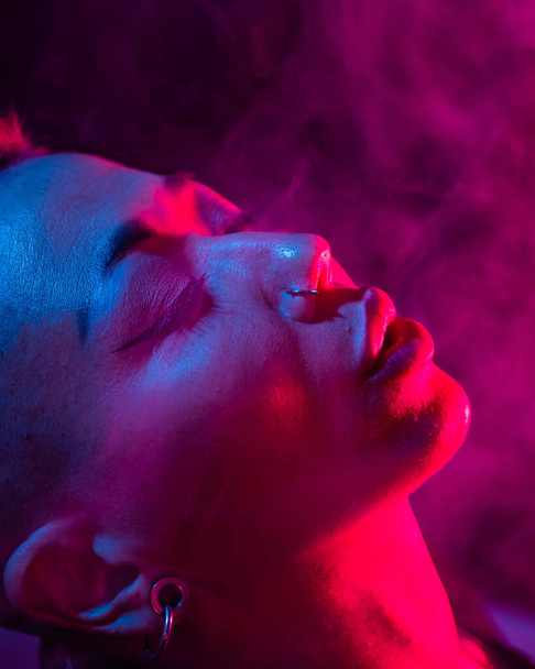 Asian woman with short haircut smoking in neon light. close-up portrait - Фото, изображение