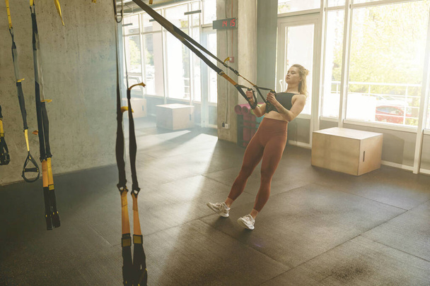 Jovem mulher ajuste formação em corda elástica trx no centro de fitness ginásio. Foto de alta qualidade - Foto, Imagem