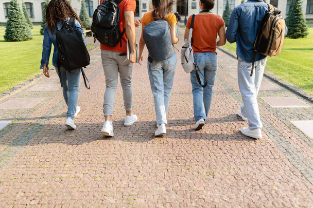 Ομάδα φοιτητών που περπατούν στο δρόμο στο κολέγιο μετά τα μαθήματα, πίσω όψη των πολυεθνικών νέων που μεταφέρουν σακίδια που πηγαίνουν στα μαθήματα, crop shot των διαφόρων πανεπιστημιακών φίλων - Φωτογραφία, εικόνα
