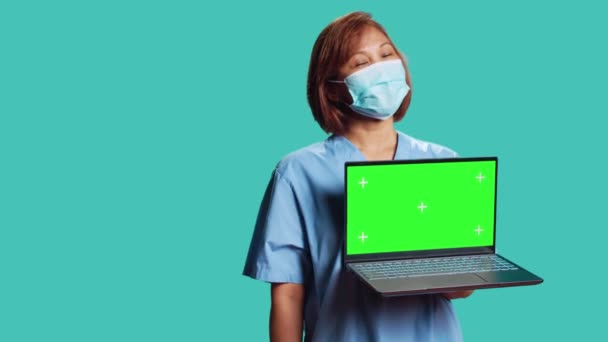 Közelíts rá egy kamera felvételre, amin a klinika alkalmazottja orvosi videót mutat a laptopon, ami a krómkulcs zöld képernyőjét mutatja. Nővérke bemutató tájékoztató egészségügyi szalag, elszigetelt stúdió háttér - Felvétel, videó