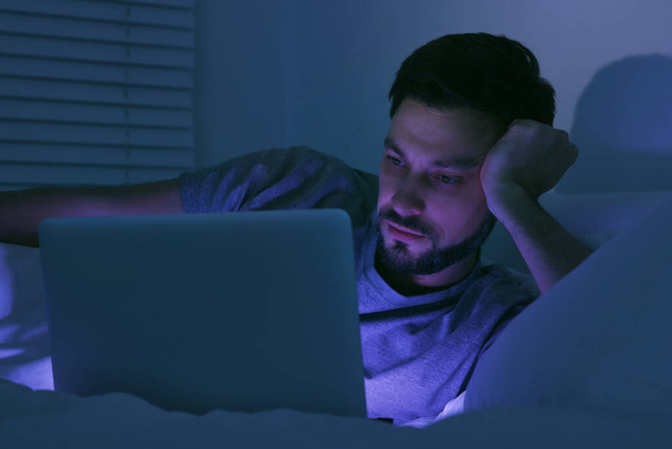 Man using laptop in bed at night. Internet addiction - 写真・画像