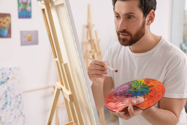 Man painting in studio. Using easel to hold canvas - Foto, Bild