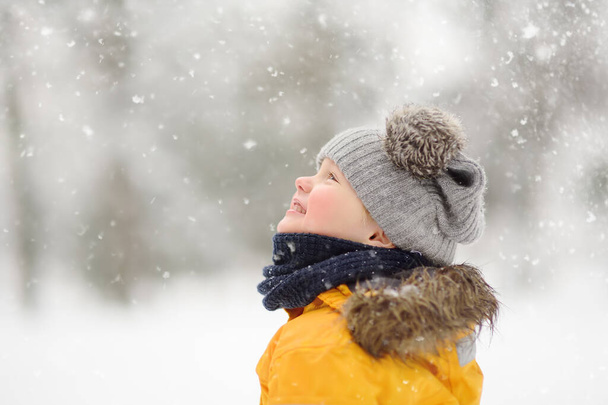 Cute little boy in yellow winter clothes walks during a snowfall. Outdoors winter activities for kids. - Photo, image