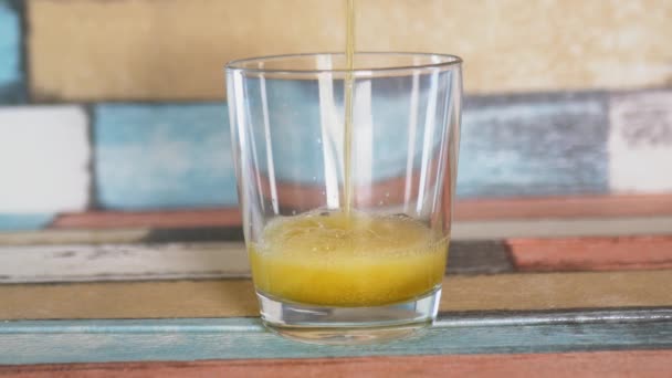 Orangefarbenes kohlensäurehaltiges Getränk wird in ein transparentes Glas auf farbigem Hintergrund gegossen. - Filmmaterial, Video