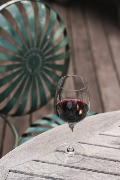Glass of red wine standing on the wooden table on the patio, cozy atmosphere - Foto, afbeelding