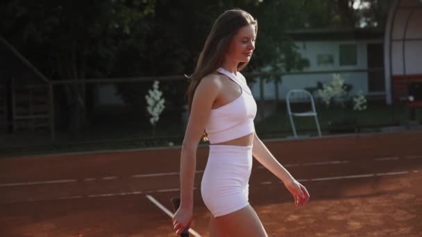 Una joven jugando al tenis en una cancha deportiva de barro. El concepto del juego de tenis - Metraje, vídeo