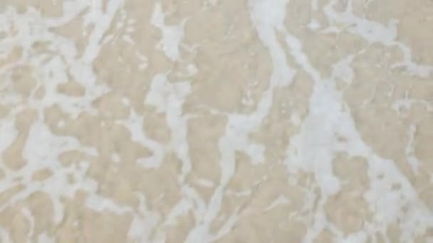 kilátás fehér homokos strand felülete textúra tenger hullám sújtotta a strandon nyáron napsütéses nap, hullám söpört a part felé fehér buborék hullámok, nyári nyaralás nyaralás háttér 4k videó. - Felvétel, videó