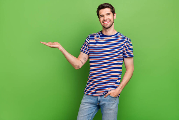 Photo of marketolog young promoter guy wear striped t shirt hold hand his company service empty space isolated on green color background. - Photo, Image