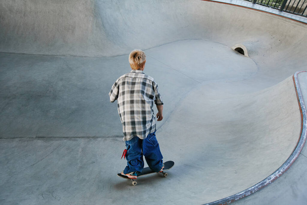 Back view of young boy riding skateboard at outdoor skatepark in urban area, copy space - Foto, Imagen