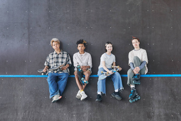Minimální široký záběr různorodé skupiny teenagerů sedících na rampě ve skateboardingu a dívajících se na kameru, kopírovací prostor - Fotografie, Obrázek
