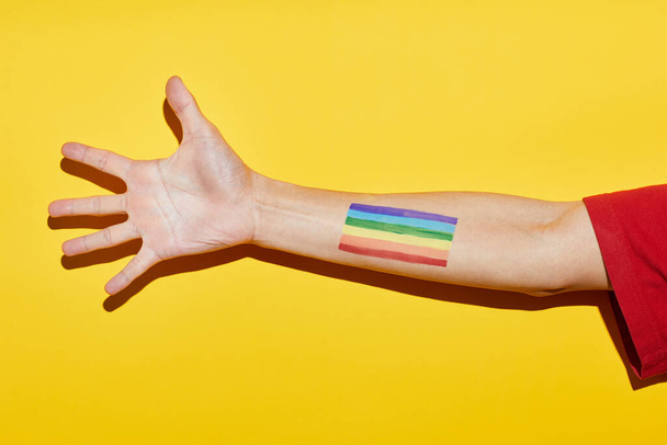 Vibrante foto amarilla del brazo con el tatuaje de la bandera del arco iris como símbolo del mes del orgullo LGBTQ - Foto, Imagen