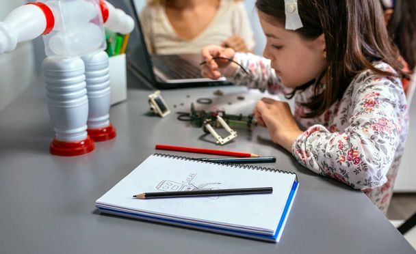 Robot dessiner par enfant sur ordinateur portable avec note de panneau solaire tandis que l'étudiant femelle connecte le fil dans le circuit électrique à la classe de robotique - Photo, image