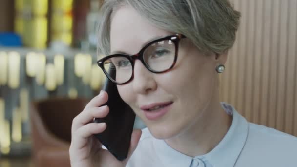 Primer plano de la mujer de negocios caucásica en gafas y camisa formal hablando por teléfono en el restaurante - Metraje, vídeo