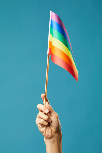 Яркий снимок женской руки с радужным флагом на синем фоне как символ гордости месяца lgbtq - Фото, изображение