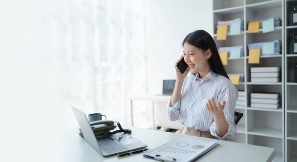 Danışman, telefonda çalışan Asyalı iş kadını şirket kârlarını artırmak için finansal iş ve pazarlama planlarını tartışıyor bilgisayar ve pazarlama planlama belgelerini kullanmaya hazır. - Fotoğraf, Görsel